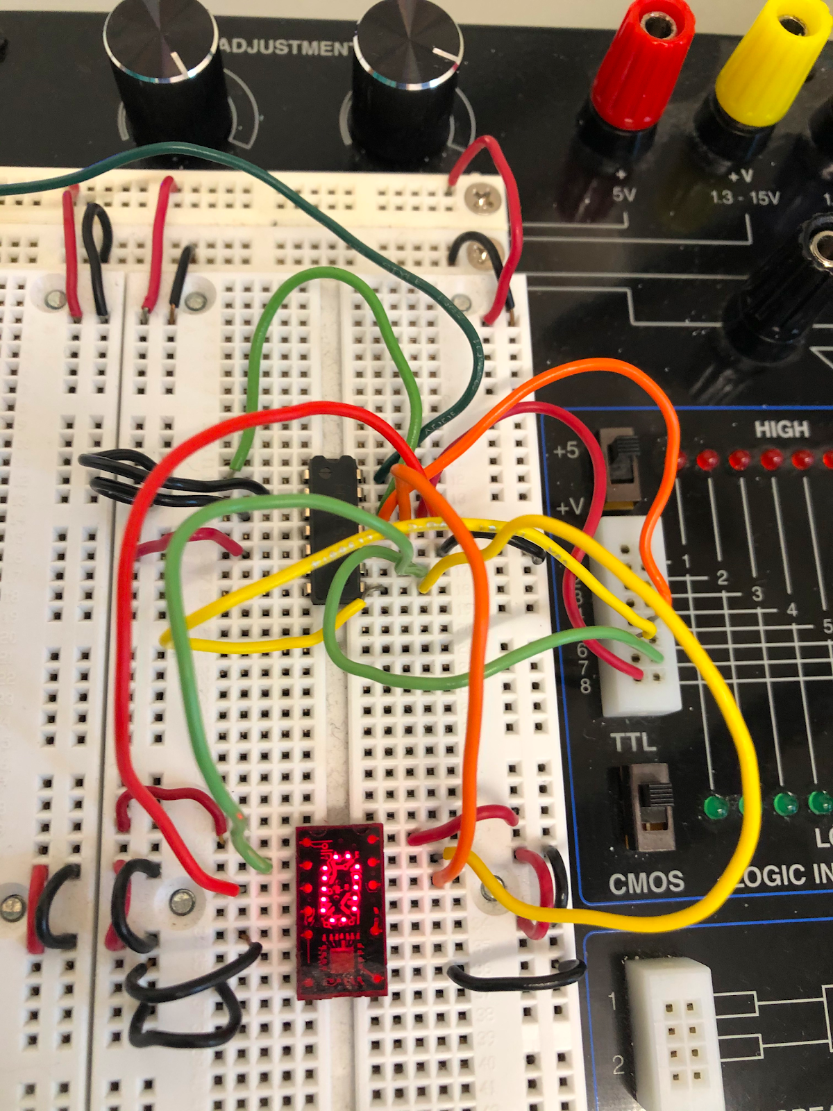 A picture of both the 7493 and the TIL311 connected on the protoboard. The 7493 sits about 10 rows above the TIL311. The 7493 is connected as shown in the picture above, but with 4 extra wires connecting pins on the 7493 to pins on the TIL311: pin 8 to pin 13, pin 9 to pin 2, pin 11 to pin 12, and pin 12 to pin 3. The other connections from the TIL311 are: pins 1 and 14 to +5V, pins 5, 7, and 8 to ground. Red LEDs built into the clear red face of the TIL311 display the digit 0, and circuit traces internal to the chip can also be seen below the clear face.