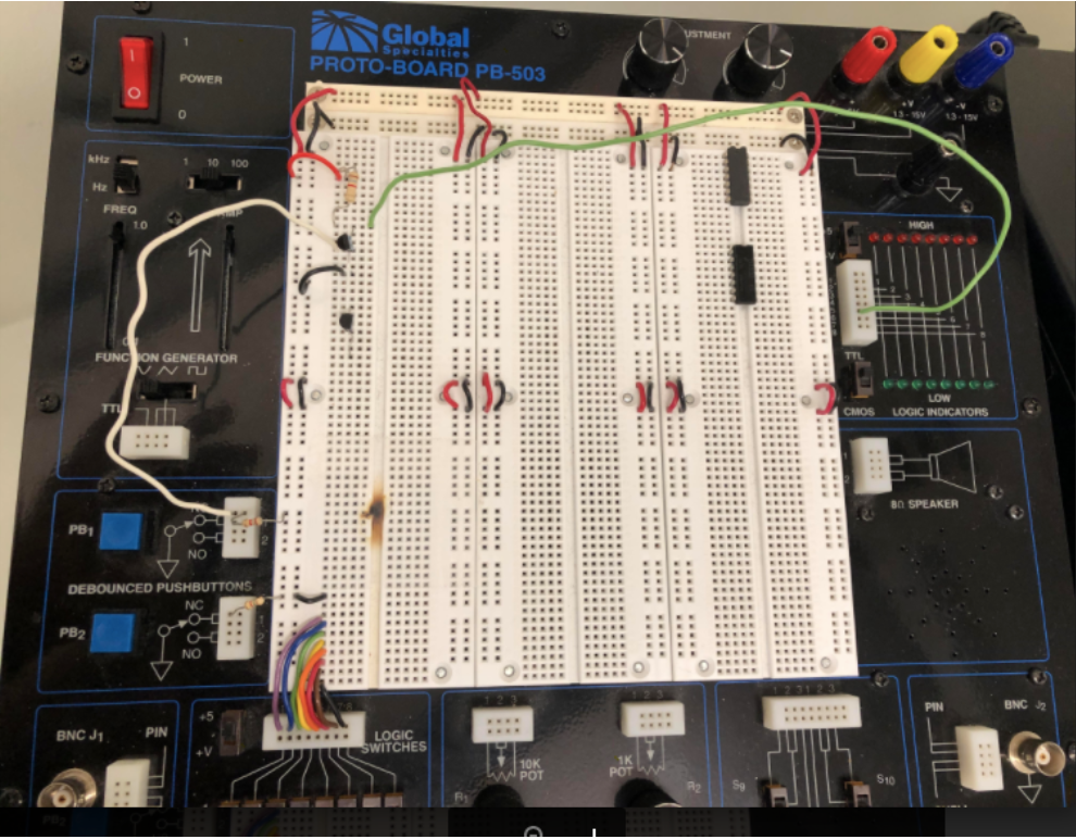 A picture of a protoboard, with some transistors, wires, and chips connected. The power switch is on the upper left, and is a red rocker-type switch which is ON when the top part is pushed down and OFF when the bottom part is pushed down. Black and red wires are connected already which connect +5V and ground to 6 sets of vertical rails going up and down the center, which is white. Each rail connects vertically underneath a series of holes which can be used to plug wires into it. In between these sets of rails are three sets of paired rows of holes, where in each row has a left and right half. The two halves are not connected to each other, but every hole on each half is connected to the other holes in the same half of the row. This allows a chip to be inserted spanning between the halves, such that each pin of the chip connects to a single row on either the left or right half. This in turn makes it easy to plug up to 4 wires into holes that will connect to a particular pin of the chip (the half-rows have 5 holes each, and the chip leg takes up one of them). Two chips are plugged into the board in this manner in the upper-right region. On the left, two transistors are plugged in, spanning across several rows. Outside the center region with the holes, there are input and output devices around the edge of the board. A function generator below the power switch on the left, two push-buttons below that, a BNC J1 connector on the bottom-left, a series of eight logic switches to the right of that bottom-left corner, 10K and 1K POT connections in the middle of the bottom, S9 and S10 switches on the right of the bottom, a BNC J2 connector on the bottom-right, an 8Ω speaker above that on the right edge, and a set of 8 logic indicator lights on the upper part of the right edge. At the top-right there are three voltage connections (+5V, +13-15V, and -13-15V) and a ground connection, with two adjustment knobs at the top. Each of these various input/output devices has its own set of holes into which wires can be connected, the push-buttons are already connected to the left-most +5V rail with resistors, and the 8 logic switches have been wired to 8 of the horizontal rows on the bottom-left of the board.