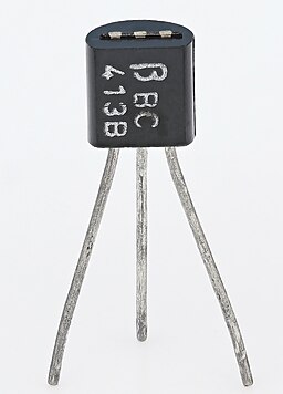 A black cylinder, truncated along one side so that it’s got one flat side and the rest of the way around it’s circular. Out of the bottom three metal “legs” come out along a line, so that one comes out of the middle and two more come out on either side (this line is parallel to the flat side of the cylinder and perpendicular to the camera angle). The legs are bent at angles so the first and last legs bend outwards along the line of the legs, while the middle leg bends away from the camera and so the ends of the three legs form a triangle, not a line.